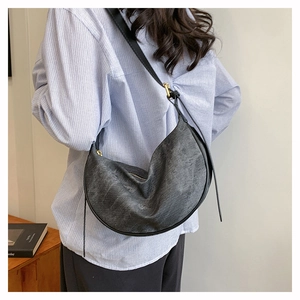 Detail of grey-black crescent crossbody bag with wide strap on a striped shirt model