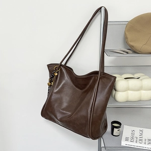 Detalle de bolso tote marrón oscuro con colgante trenzado y correas largas de hombro