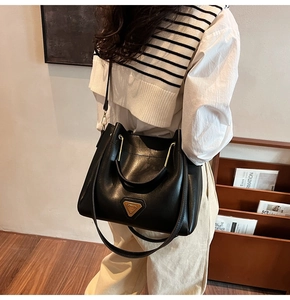 Détail du sac seau noir mat avec logo triangle doré et poignée en métal en forme de U