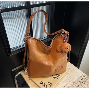 Detail of caramel brown tote bag showing mixed leather textures and cute plush dog charm