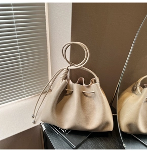 Close-up of beige leather drawstring bucket bag with litchi texture and knot handle detail