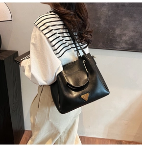 Détail d'un sac seau en cuir noir avec logo triangle doré porté à l'épaule