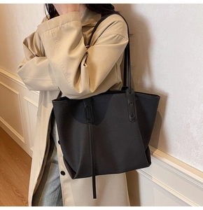 Close-up of the woven texture and minimalist vertical leather straps on a black tote bag