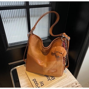 Close-up of vintage brown patchwork tote bag with plush puppy pendant and textured PU leather