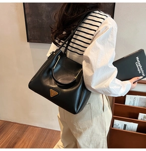 Détail du sac seau en cuir noir avec logo triangulaire doré et finitions métalliques