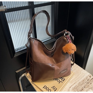 Detail of dark brown patchwork tote bag with plush puppy charm on marble base