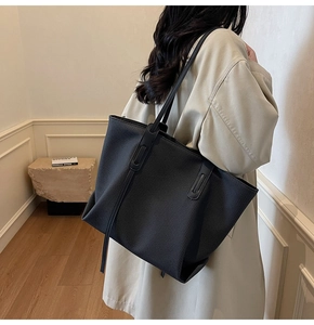 Detailed view of black woven tote bag worn with a beige trench coat for a minimalist look