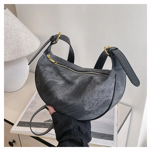 Detail of washed denim crescent bag with gold zipper and adjustable leather strap