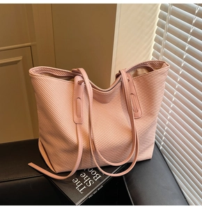 Detail view of pink woven tote bag with dual straps and zipper on leather surface