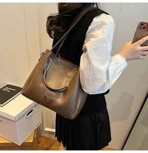 Détail du sac seau en cuir marron avec poignée en arche métallique et plaque logo