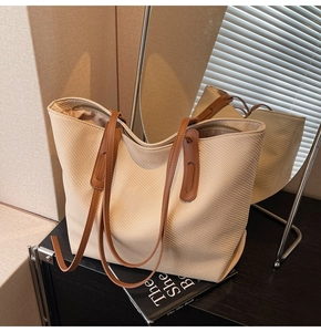 Detail of beige woven tote bag with brown leather straps and smooth metal zipper