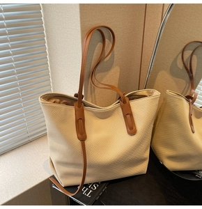 Close-up of beige woven tote bag with brown leather straps on a decorative book