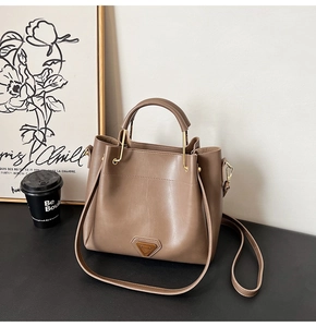 Détail d'un sac seau marron avec plaque triangle dorée et poignée structurée chic