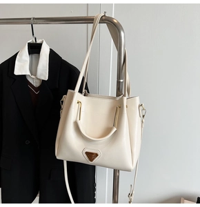 Détail d'un sac trapèze beige avec poignées en métal doré sur fond de blazer noir chic