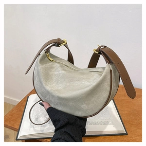 Detail of light green canvas crescent bag with brown leather trim on a wooden table