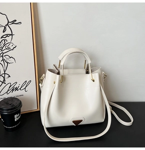 Détail du sac seau crème montrant la plaque logo en métal et la texture du cuir lisse