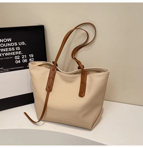Detail of beige woven tote bag with dark brown leather straps and metal zipper closure