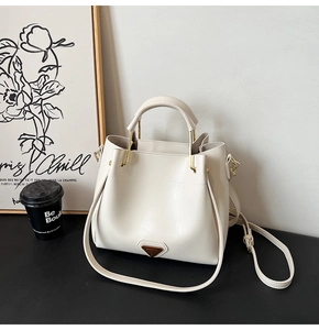 Gros plan d'un sac seau crème avec logo triangulaire en métal et bandoulière amovible
