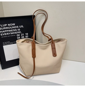 Close-up of beige woven tote bag with brown leather straps and metal zipper detail