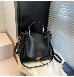 Détail d'un sac seau en cuir noir avec logo triangulaire argenté sur tissu blanc
