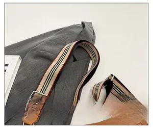 Detail of adjustable striped fabric shoulder strap on a brown pebbled leather saddle bag