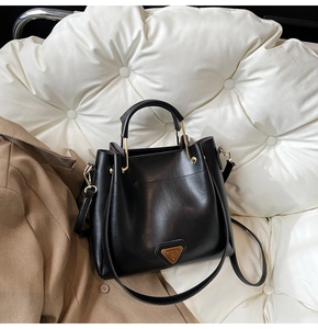 Détail d'un sac seau noir en similicuir avec quincaillerie dorée sur un canapé blanc