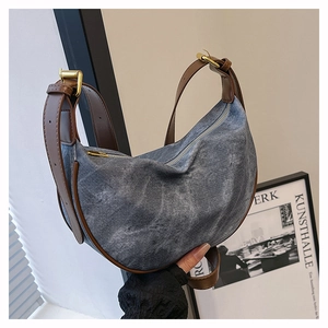 Detail of blue denim crescent bag with brown leather trim and adjustable shoulder strap