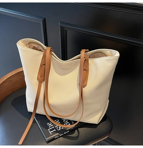 Close-up of cream woven tote bag texture with brown leather straps and metal zipper detail