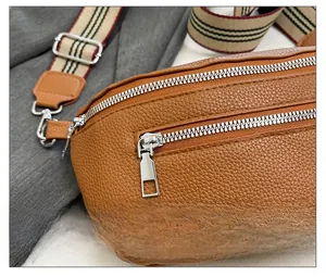 Detail of soft brown lychee grain leather crossbody bag with silver zipper and striped strap