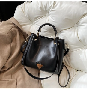Gros plan du sac seau en cuir noir mat avec logo triangulaire doré et finitions chic