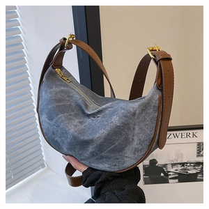 Detail of blue denim crescent bag with brown leather trim and golden zipper