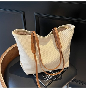 Detail shot of beige woven tote bag featuring brown leather straps and gold zipper closure