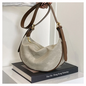 Close-up of beige suede crescent bag with brown leather strap and gold hardware detail