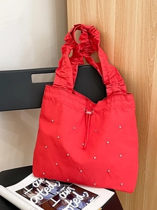 Rote Schultertasche mit Falten, Strasssteinen und Kordelzug, hängend an einem Stuhl