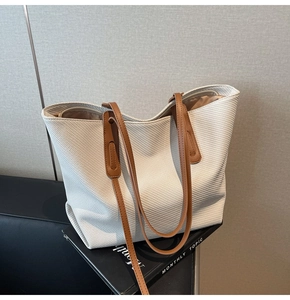 Close-up of the diagonal woven texture and brown leather handle on a cream tote bag