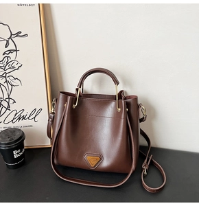 Détail d'un sac seau en cuir marron foncé avec finitions dorées dans un décor épuré