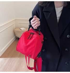 Detail van rode nylon mini-tas met zwart-wit gedraaid handvat en metalen logo