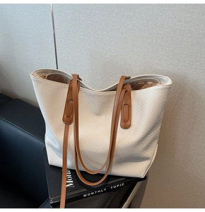 Detail of cream woven tote bag showing brown leather straps and smooth zipper closure