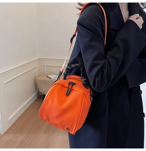 Close-up van een feloranje mini crossbodytas in schelpvorm gedragen door een model