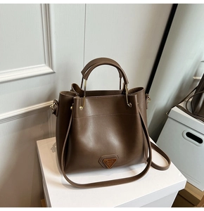 Détail du sac seau en cuir mat marron foncé avec logo métallique doré et anneaux