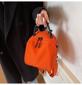 Detail van de feloranje mini rugzak met gevlochten touwhandvat en zwarte ritsen