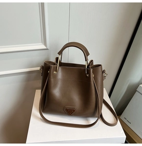 Détail du sac seau marron avec finitions dorées et logo triangulaire emblématique
