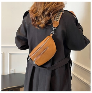 Detail of soft brown lychee leather saddle bag featuring a textured wide woven strap