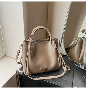 Détail d'un sac à main trapèze en cuir taupe posé sur une surface en bois sombre élégant