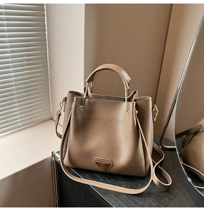 Gros plan du sac seau en cuir taupe avec plaque triangulaire métallique et poignée chic