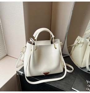 Détail d'un sac seau crème avec poignée métallique et plaque triangulaire sur table
