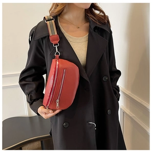 Close-up of red lychee texture saddle bag with striped wide shoulder strap worn on coat