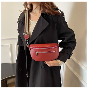 Detail of red pebbled leather saddle bag with striped shoulder strap worn on a black coat
