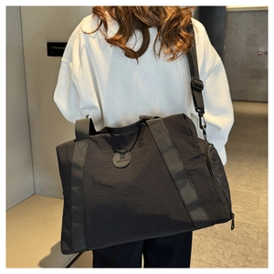 Rear view of a model carrying a large black nylon travel bag in a modern corridor