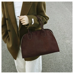 Street view of a burgundy suede Boston handbag held by a model in an olive wool coat
